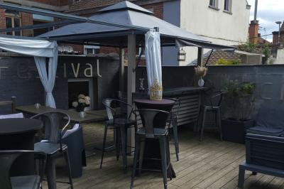 Terrasse en bois avec fauteuils, pergola à rideaux blancs, plantes en pot et mur en briques en arrière-plan.