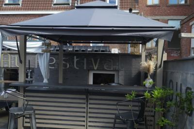 Terrasse en bois avec fauteuils, pergola à rideaux blancs, plantes en pot et mur en briques en arrière-plan.