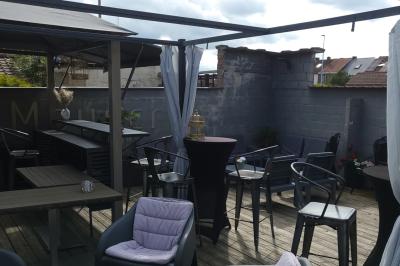 Terrasse en bois avec fauteuils, pergola à rideaux blancs, plantes en pot et mur en briques en arrière-plan.