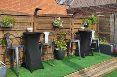 Terrasse en bois avec fauteuils, pergola à rideaux blancs, plantes en pot et mur en briques en arrière-plan.