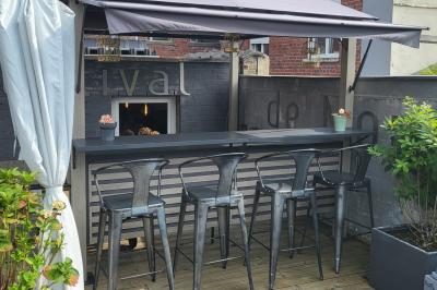 Terrasse en bois avec fauteuils, pergola à rideaux blancs, plantes en pot et mur en briques en arrière-plan.