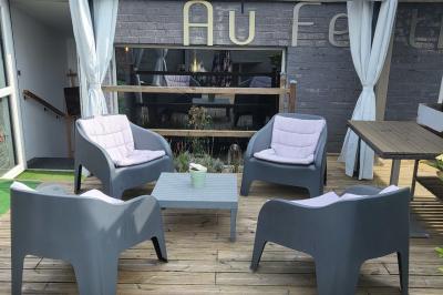 Terrasse en bois avec fauteuils, pergola à rideaux blancs, plantes en pot et mur en briques en arrière-plan.