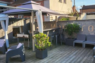 Terrasse en bois avec fauteuils, pergola à rideaux blancs, plantes en pot et mur en briques en arrière-plan.