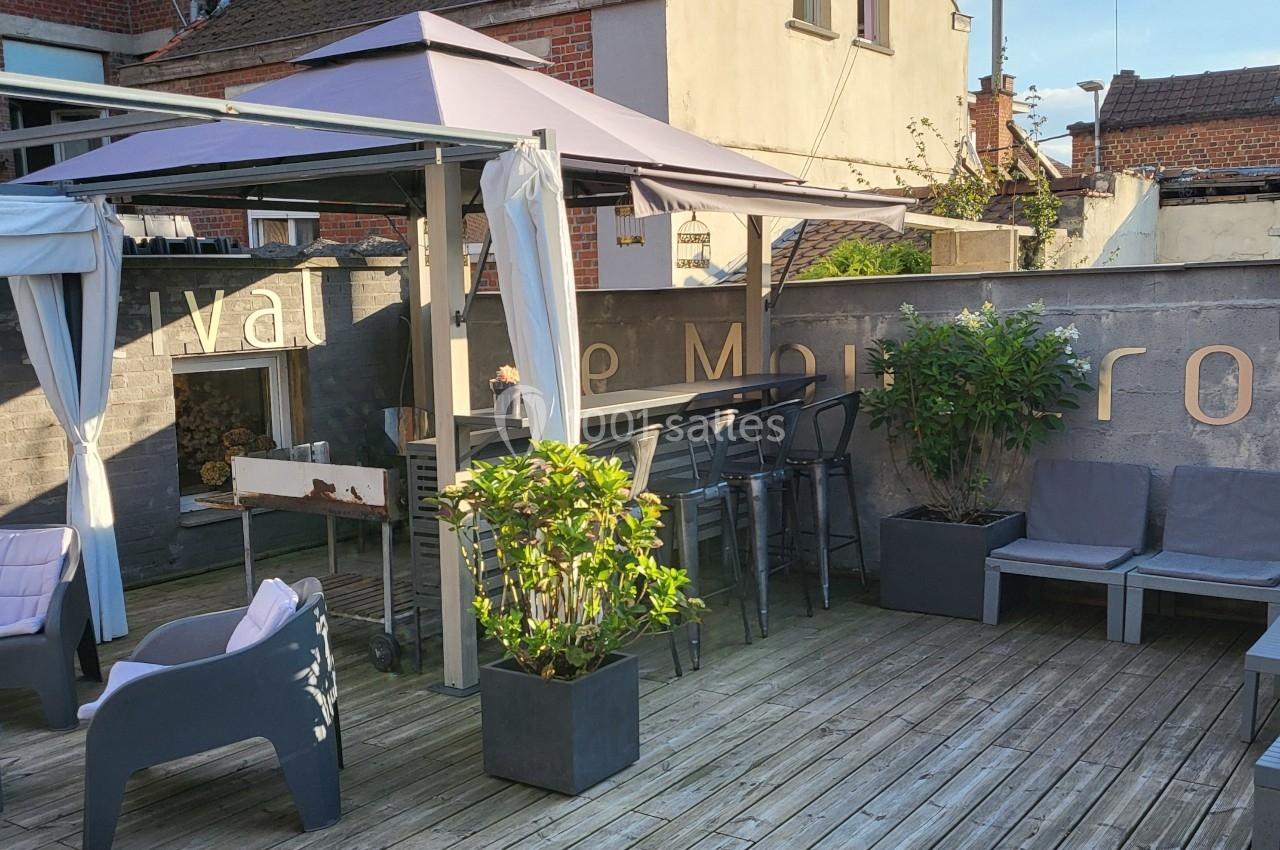 Terrasse en bois avec mobilier de jardin, pergola, plantes en pots et mur en arrière-plan.