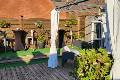 Terrasse en bois avec fauteuils, pergola à rideaux blancs, plantes en pot et mur en briques en arrière-plan.