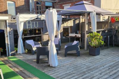 Terrasse en bois avec fauteuils, pergola à rideaux blancs, plantes en pot et mur en briques en arrière-plan.