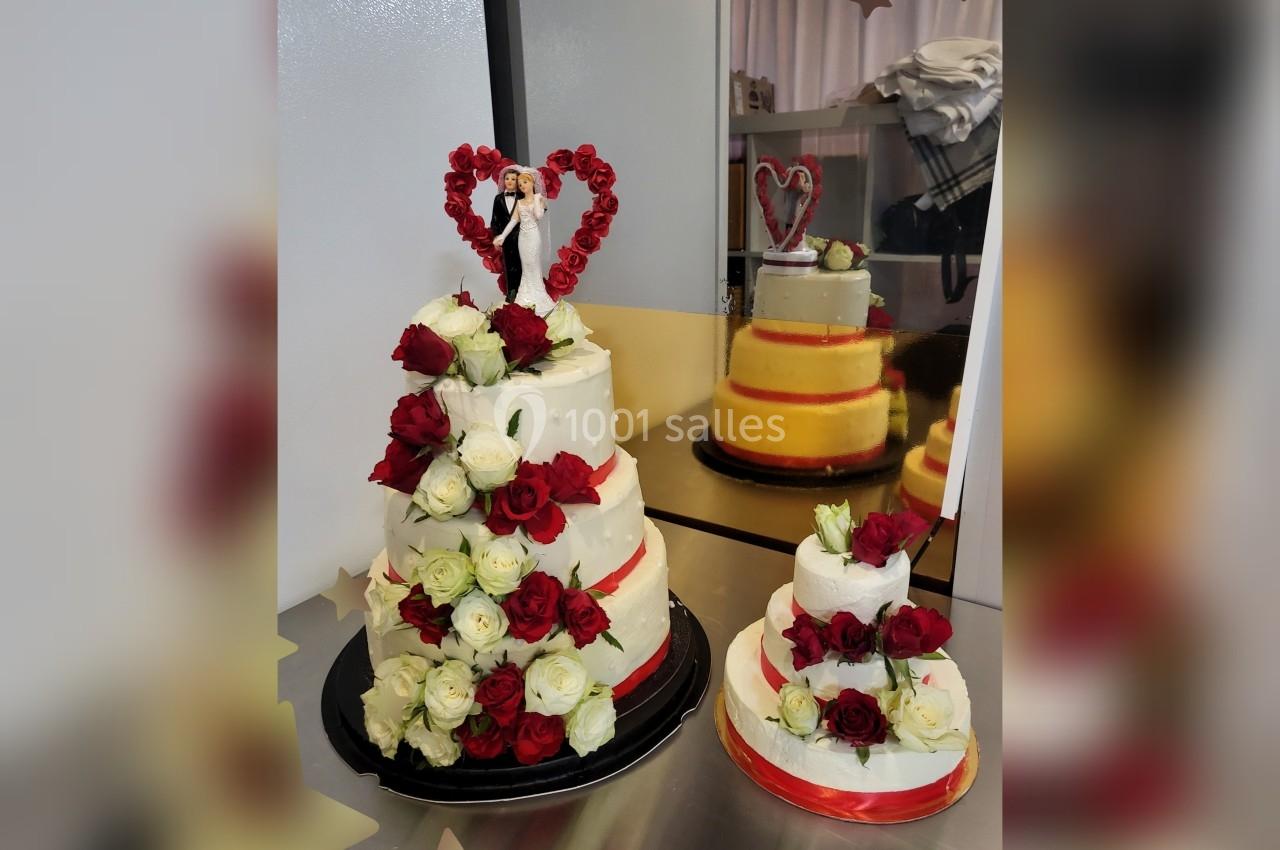 Deux gâteaux de mariage décorés de roses rouges et blanches, avec une figurine de couple au sommet du plus grand.
