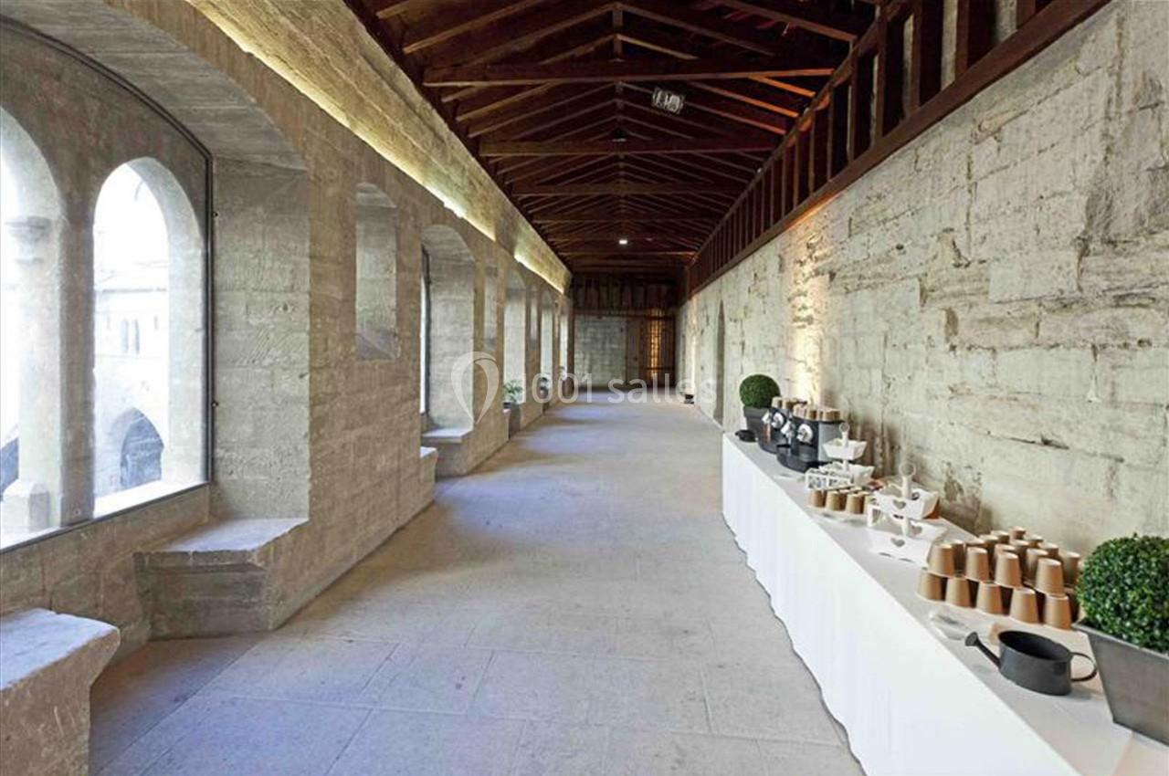 Un couloir en pierre avec des arches vitrées à gauche et une table de service dressée à droite.