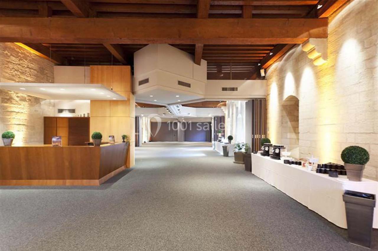 Salle spacieuse avec plafond en bois, murs en pierre, comptoir en bois et tables dressées sur la droite.