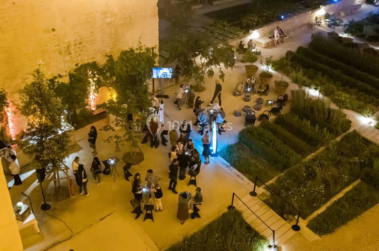 Vue nocturne d'un jardin avec des invités rassemblés lors d'un événement, éclairé par des lumières chaleureuses.