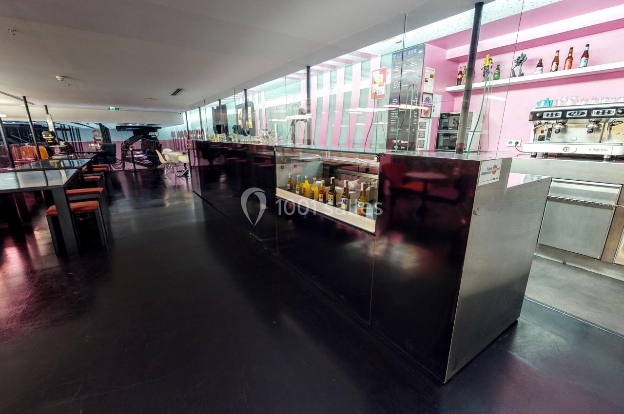 Comptoir de cafétéria moderne avec vitrines, boissons et machines à café, dans un espace lumineux aux tons roses.