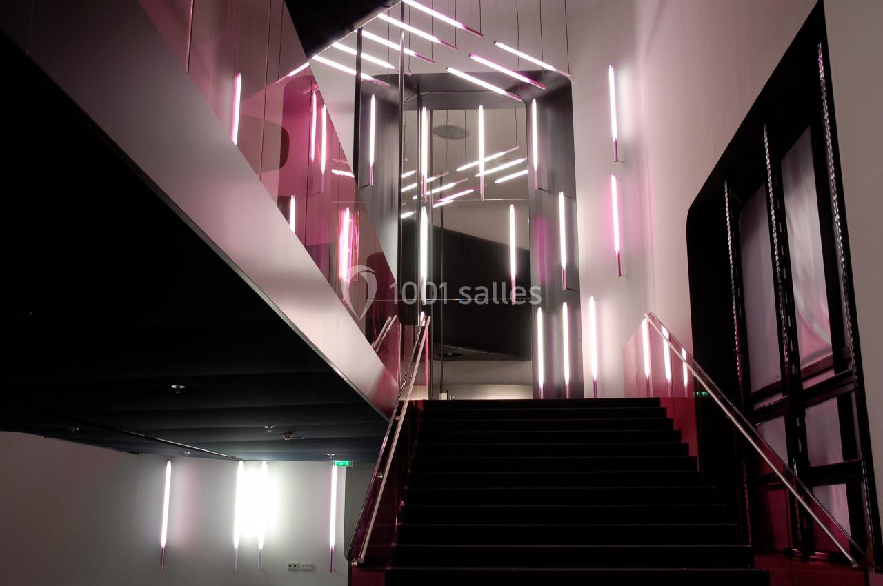 Escalier moderne avec des rampes en verre et un éclairage néon rose et blanc dans un intérieur sombre.