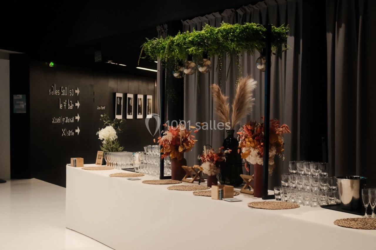 Table de réception décorée avec des fleurs, des plantes suspendues et des verres disposés sur des sets en rotin.