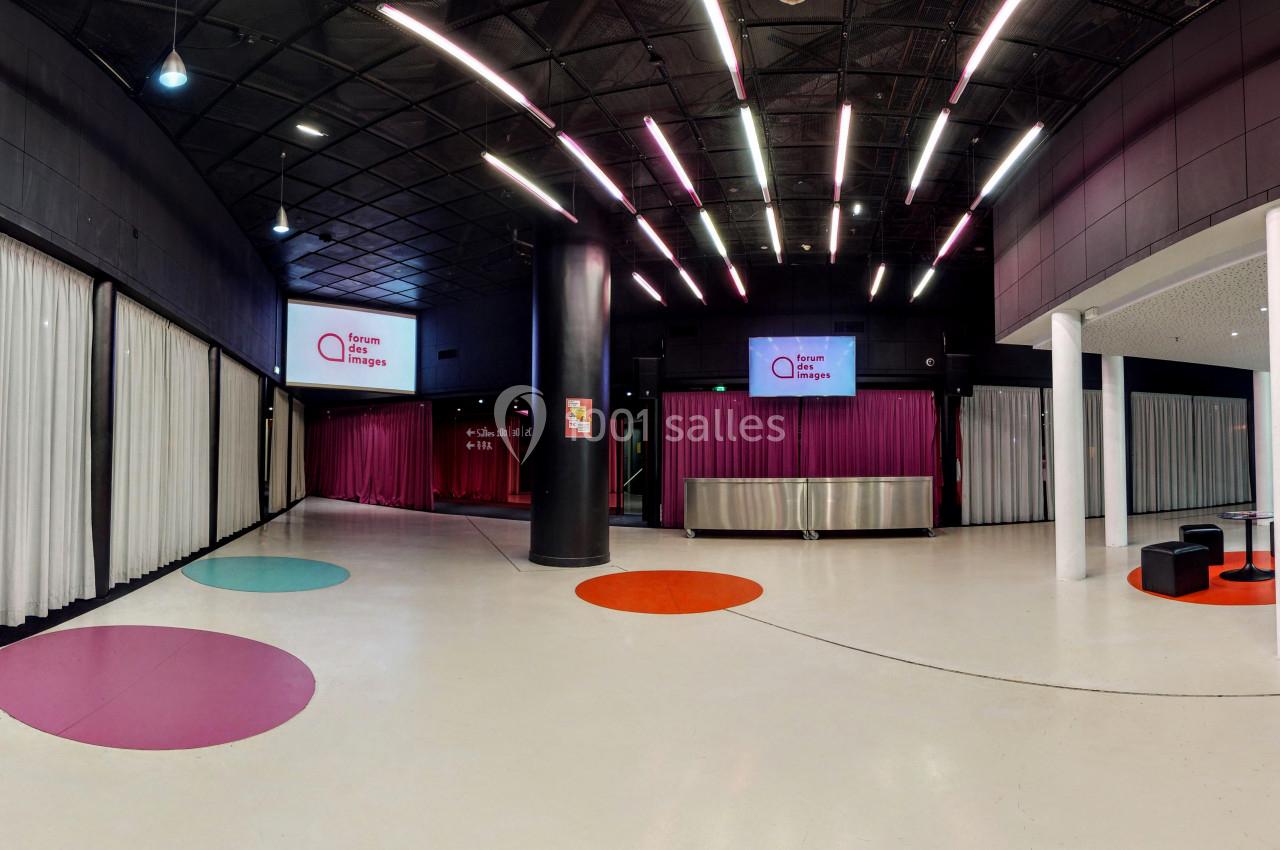 Hall moderne avec sol clair, rideaux blancs, colonnes noires, écrans suspendus et touches de couleurs au sol.