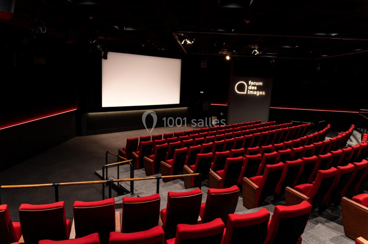 Salle de cinéma vide avec des rangées de fauteuils rouges, un écran blanc et un panneau lumineux indiquant ’Forum des images…