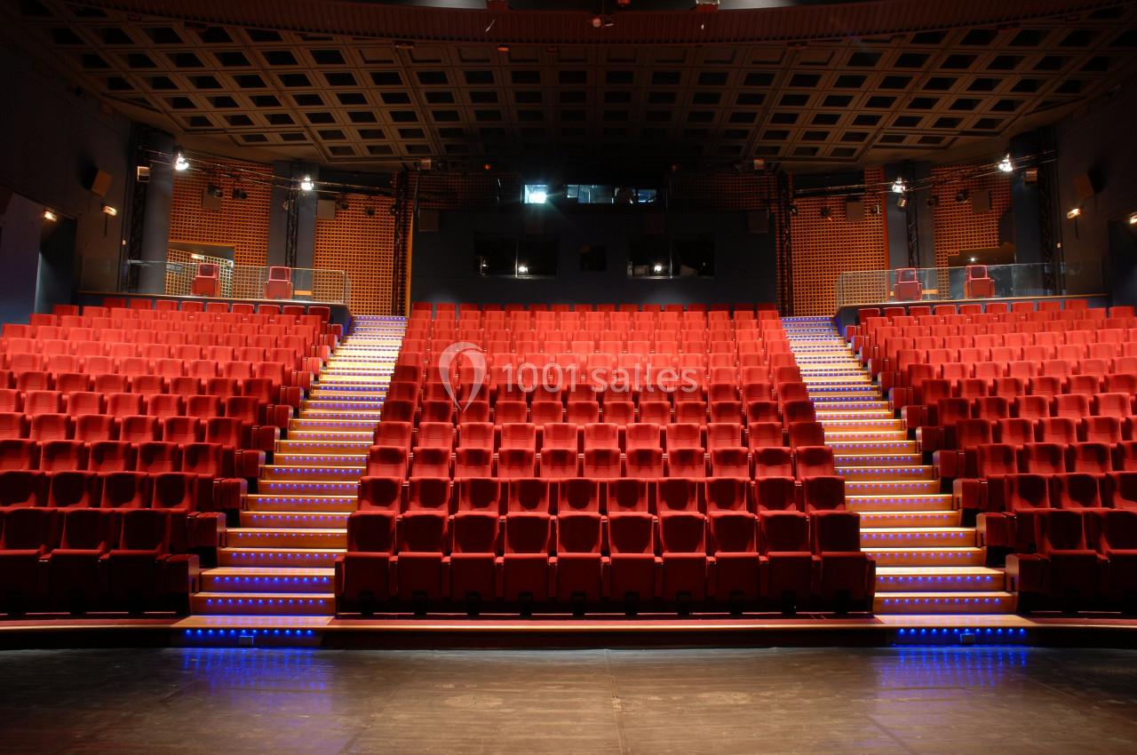 Salle de théâtre vide avec des rangées de sièges rouges et un éclairage tamisé.