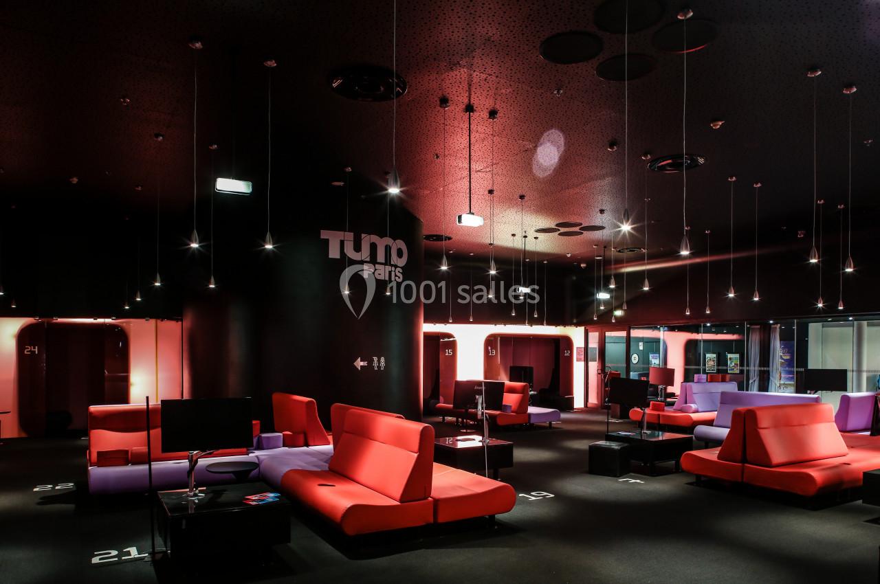 Espace intérieur moderne avec canapés colorés, éclairage suspendu et logo ’TUMO Paris’ sur un mur noir.