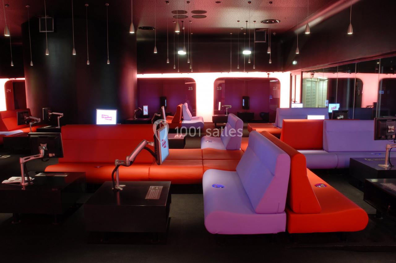 Salle moderne avec des banquettes rouges et violettes, postes informatiques individuels et éclairage tamisé.