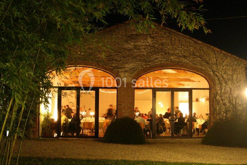 Façade vitrée d'un bâtiment en pierre éclairé de nuit, avec des personnes dînant à l'intérieur.