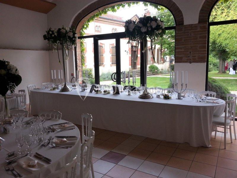 Grande table de réception décorée avec des fleurs et des chandeliers, disposée dans une salle lumineuse avec vue sur un…