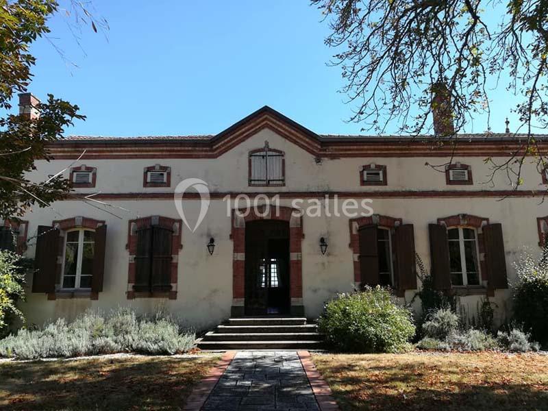 Façade d'une maison ancienne avec volets en bois, entourée de végétation sous un ciel dégagé.
