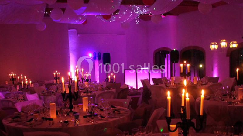 Salle de réception décorée avec des tables dressées, éclairage tamisé et bougies allumées pour une ambiance festive.