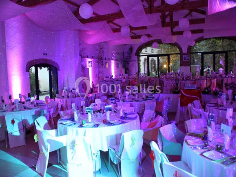 Salle de réception décorée avec des tables rondes dressées, éclairage violet et guirlandes suspendues.