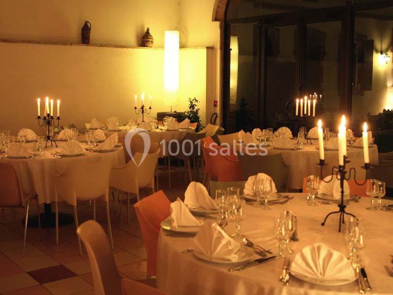 Salle de réception élégamment décorée avec des tables rondes, nappes blanches, chandeliers et lumière tamisée.