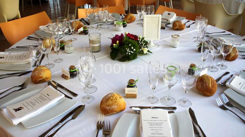 Table dressée avec nappes blanches, couverts, verres, petits pains, menus et centre de table floral.