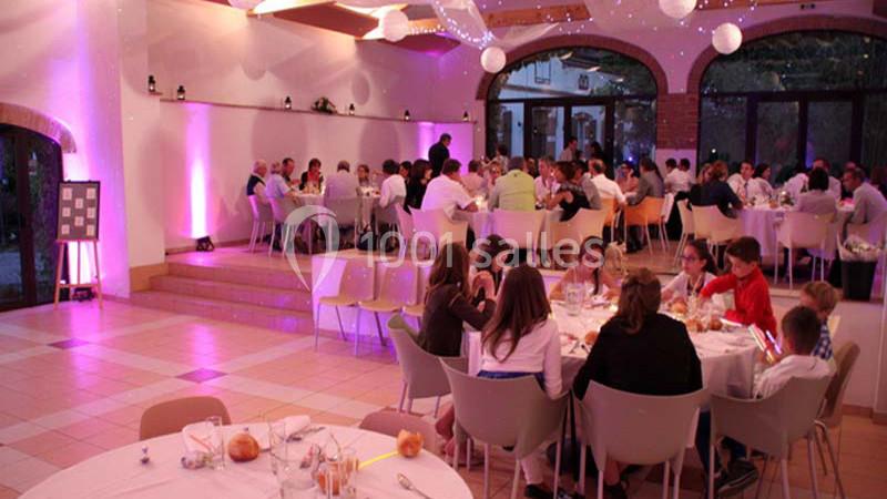 Salle de réception éclairée en rose avec des invités assis à des tables rondes lors d'un événement festif.
