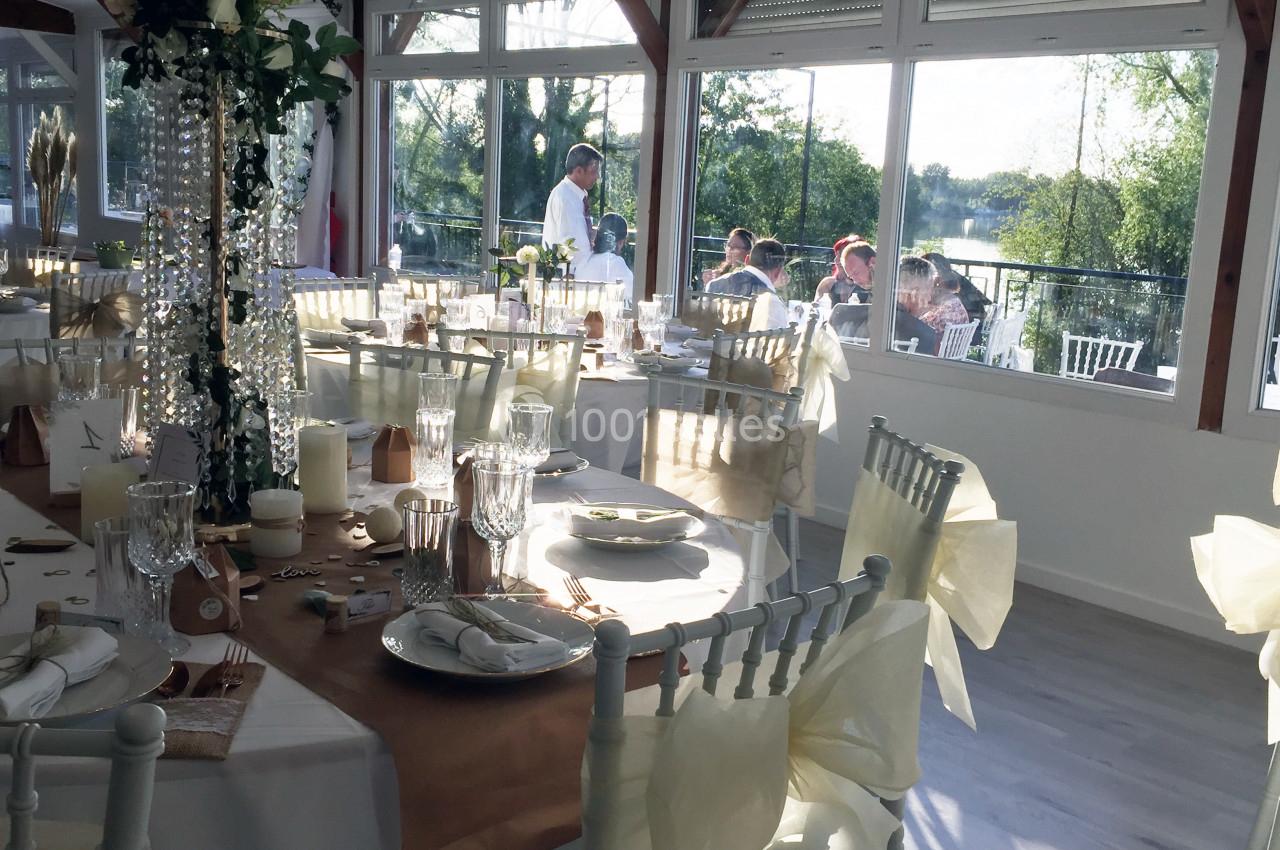 Salle de réception décorée avec des tables élégantes, nappes blanches et vue sur un paysage verdoyant à travers de grandes…