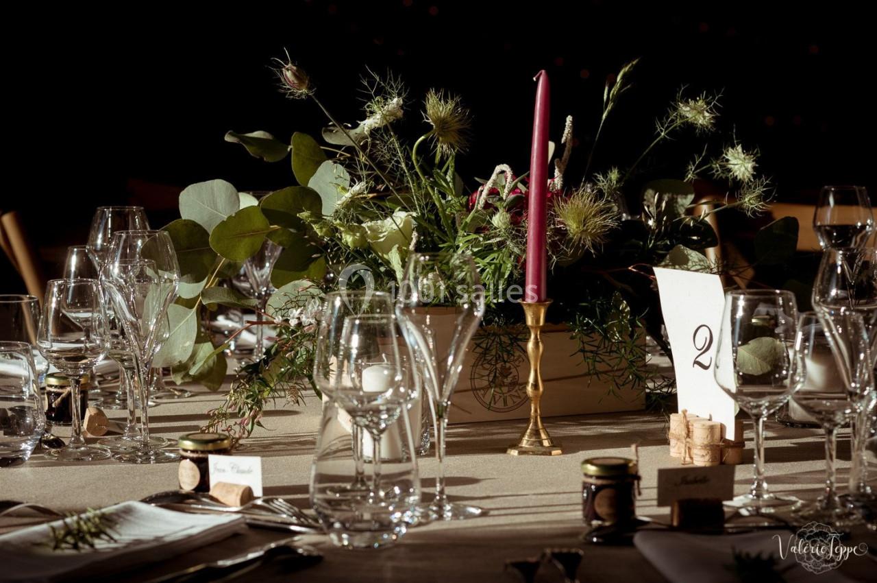 Table élégamment dressée avec des verres, des couverts, un centre de table floral et une bougie rouge sur un chandelier doré.