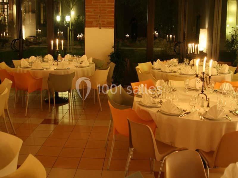 Salle de restaurant élégamment décorée avec des tables rondes dressées, éclairée par des chandeliers et une lumière tamisée.