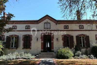 Façade d'un bâtiment en pierre avec grandes fenêtres, tables dressées à l'extérieur et tente blanche sur la droite.