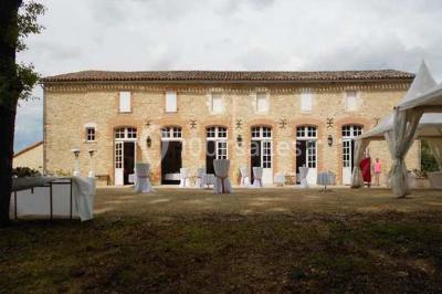 Façade d'un bâtiment en pierre avec grandes fenêtres, tables dressées à l'extérieur et tente blanche sur la droite.