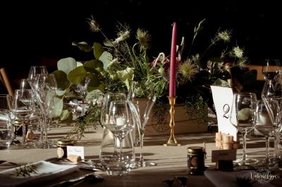 Table décorée avec des verres, un centre de table floral, une bougie rouge et une carte numérotée.