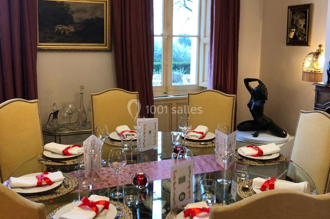 Salle à manger élégante avec table ronde dressée, nappes blanches, rubans rouges et décoration raffinée.