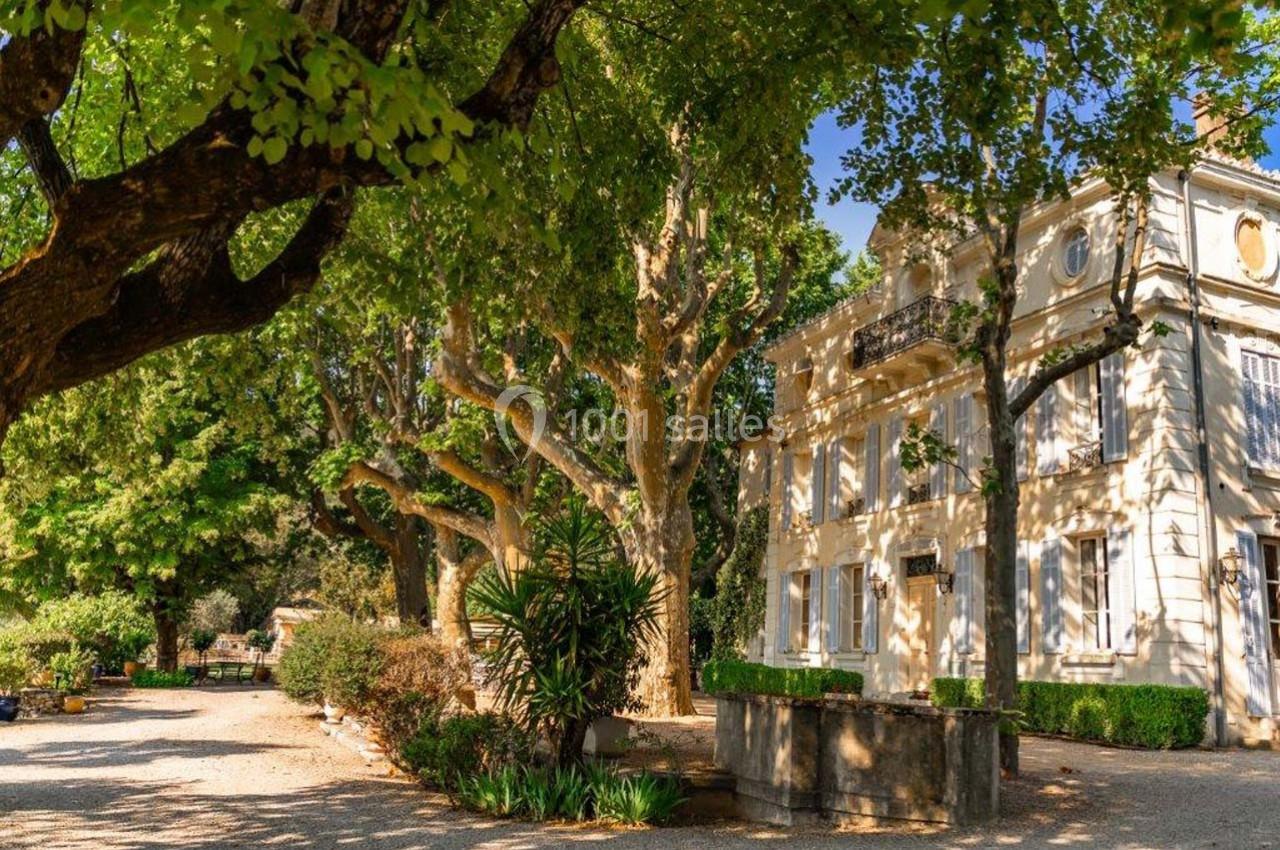 Façade d'une maison blanche entourée d'arbres et de végétation dans un jardin ensoleillé.