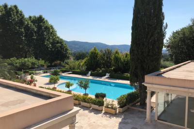 Vue sur un jardin verdoyant avec des arbres et des collines en arrière-plan sous un ciel dégagé.