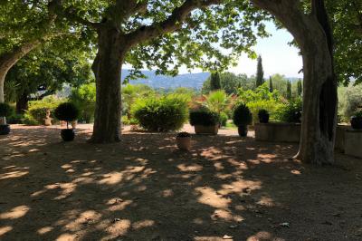 Vue sur un jardin verdoyant avec des arbres et des collines en arrière-plan sous un ciel dégagé.
