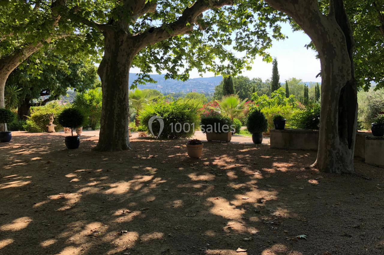 Allée ombragée bordée d'arbres et de plantes en pots, avec vue sur un paysage vallonné en arrière-plan.