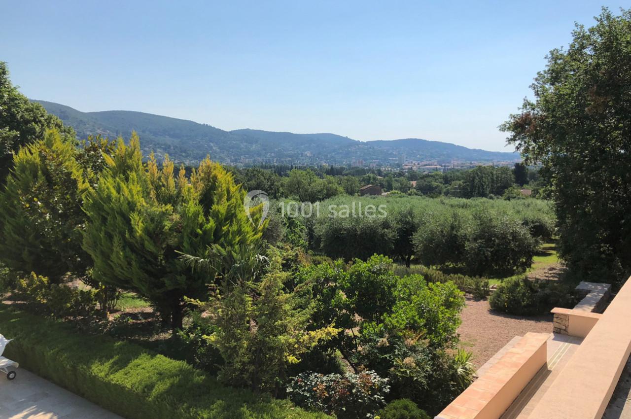 Vue sur un jardin verdoyant avec des arbres et des collines en arrière-plan sous un ciel dégagé.