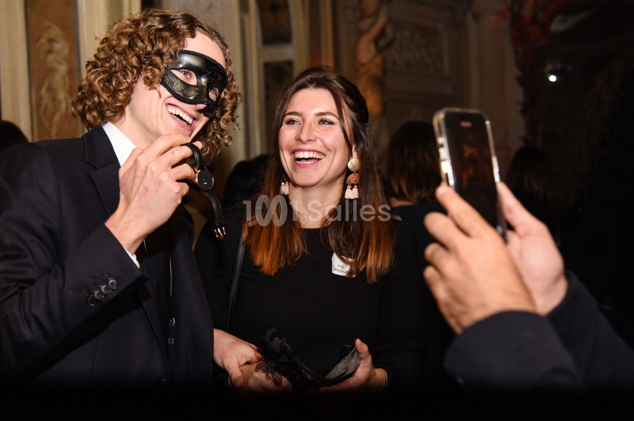 Un homme masqué et une femme souriante posent pour une photo lors d'un événement festif en intérieur.