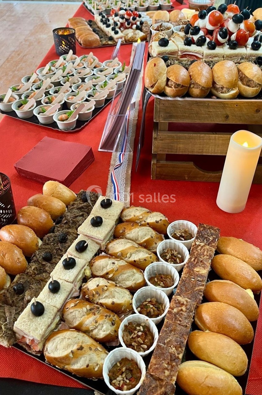 Buffet avec assortiments de pains garnis, verrines, mini-sandwichs et décorations sur une nappe rouge.