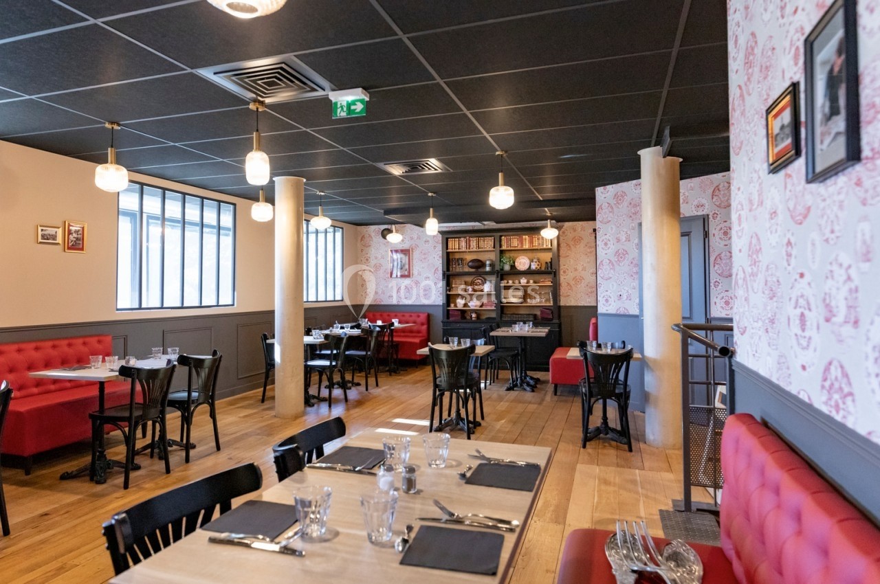 Salle de restaurant lumineuse avec tables dressées, banquettes rouges, étagères décoratives et parquet en bois clair.