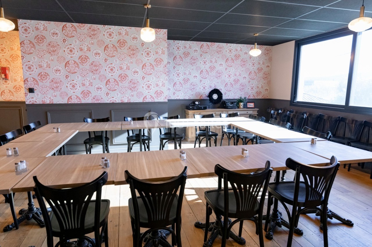 Salle de réunion lumineuse avec tables disposées en U, chaises noires et mur décoré de motifs floraux.