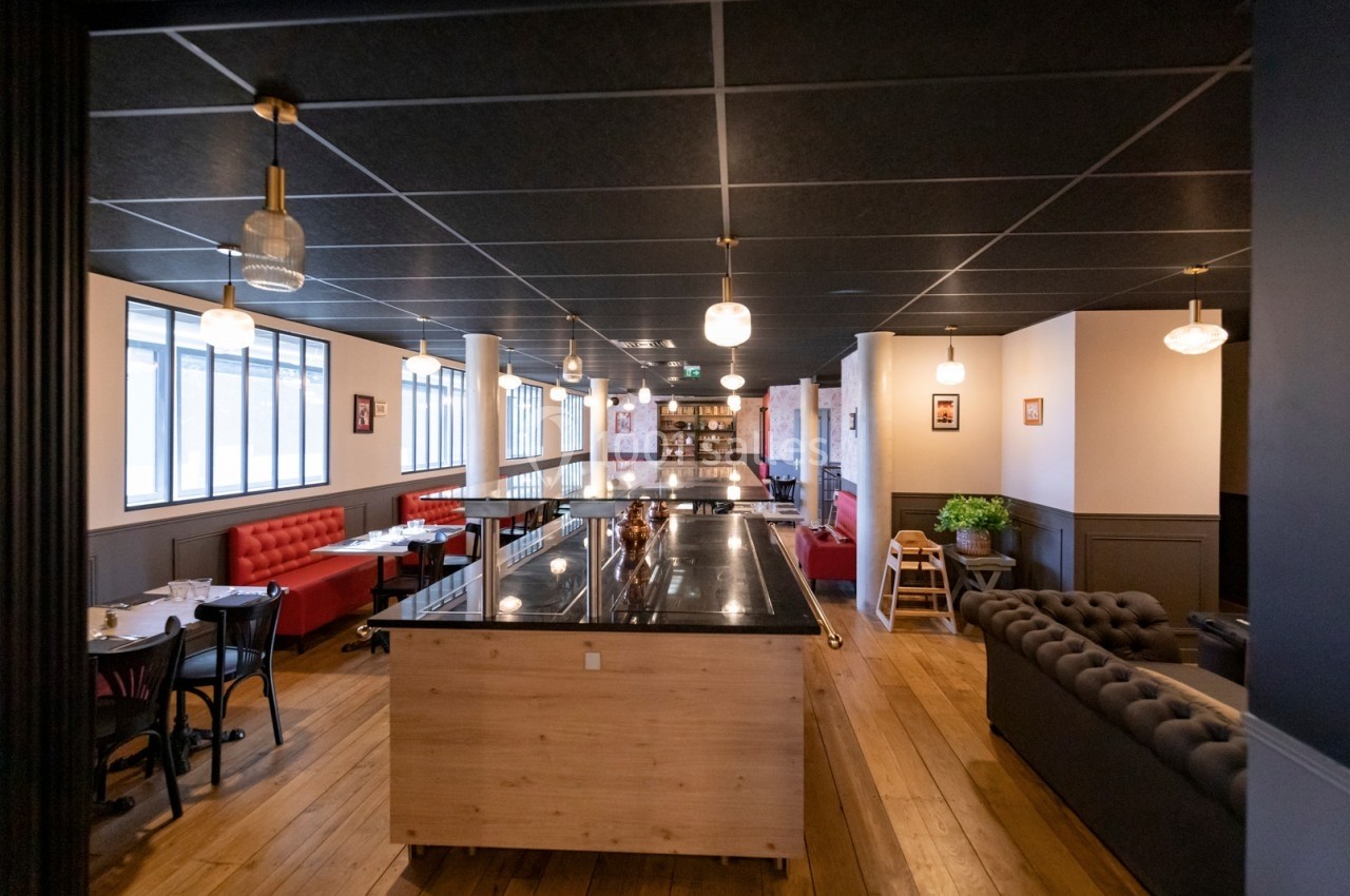 Intérieur d'un restaurant moderne avec tables, banquettes rouges, comptoir central en bois et luminaires suspendus.