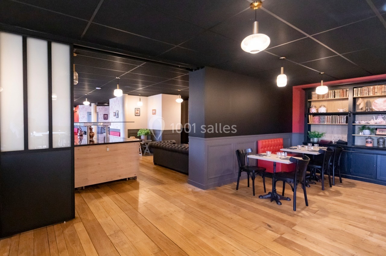 Salle de restaurant lumineuse avec parquet en bois, tables dressées, étagères décoratives et banquette rouge.