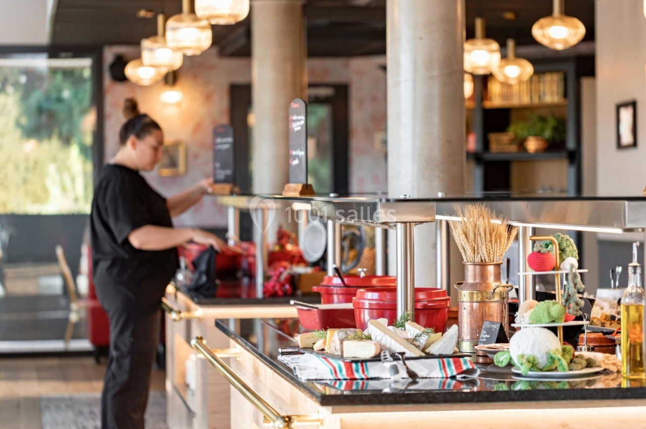 Buffet varié avec plats et légumes frais, une personne se sert dans un cadre lumineux et moderne.