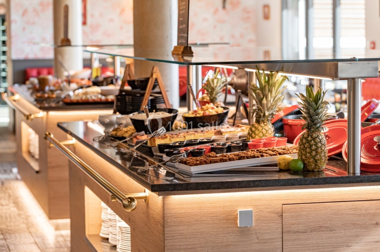 Buffet varié avec fruits, plats chauds et froids, présenté sur un comptoir en bois dans un espace lumineux.